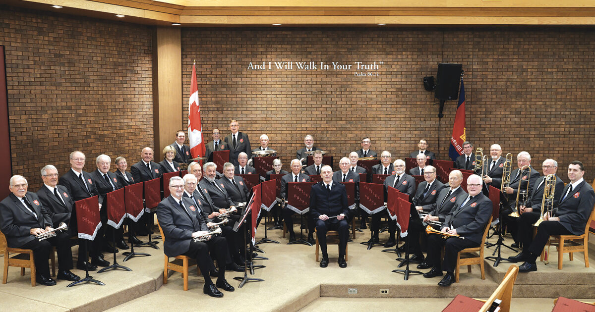 A picture of the Jubilee Brass Band. All members are in uniform and are seated ready to preform.  